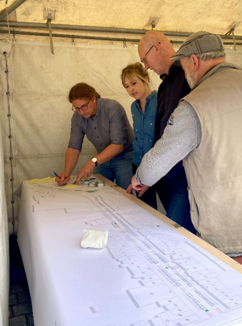 Medewerkers van Stad Mechelen en buurtbewoners staan gebogen over het straatplan