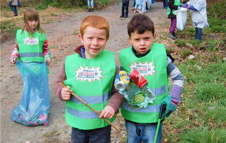 Een klas met kinderen ruimt zwerfvuil op in fluo hesjes.