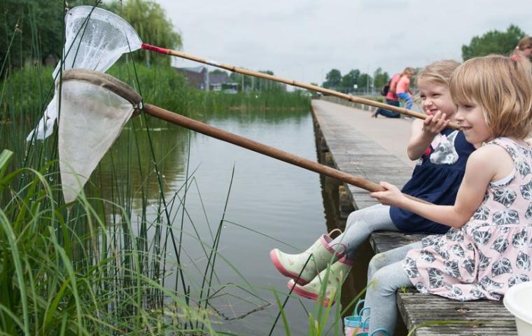 Kinderen zitten aan de wanterkant met een insectennet in de aanslag