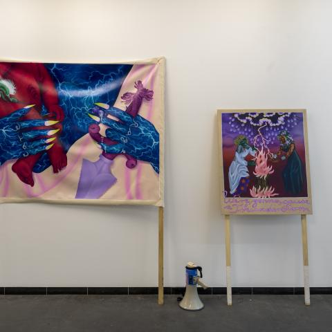 Twee spandoeken met op de één grote blauwe handen en op ander 2 'vrouwen' rond een vuur 