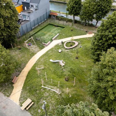 Een luchtfoto van speelplein Berkenhof. Er is een voetbalveld in kunstgras, schommel, zitbanken, picknickbanken waar ook personen in een rolstoel makkelijk kunnen aanschuiven, een touwenparcours ...