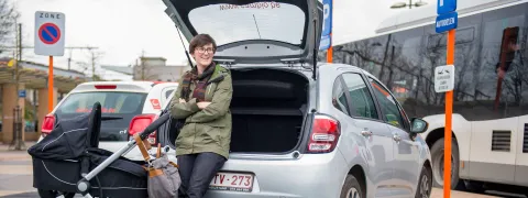 Een persoon staat bij haar deelwagen.