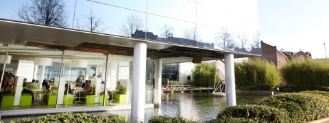 Op de foto zie je een bedrijf met grote, spiegelende ramen en beneden een kantine. 