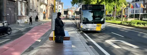 Een persoon wacht op de bus aan de bushalte