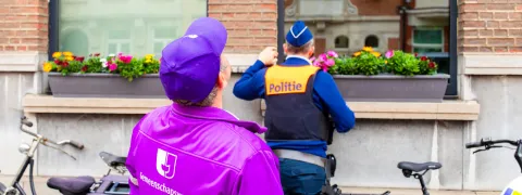 Gemeenschapswacht en politieagent houden toezicht bij een woning van iemand die op vakantie is.